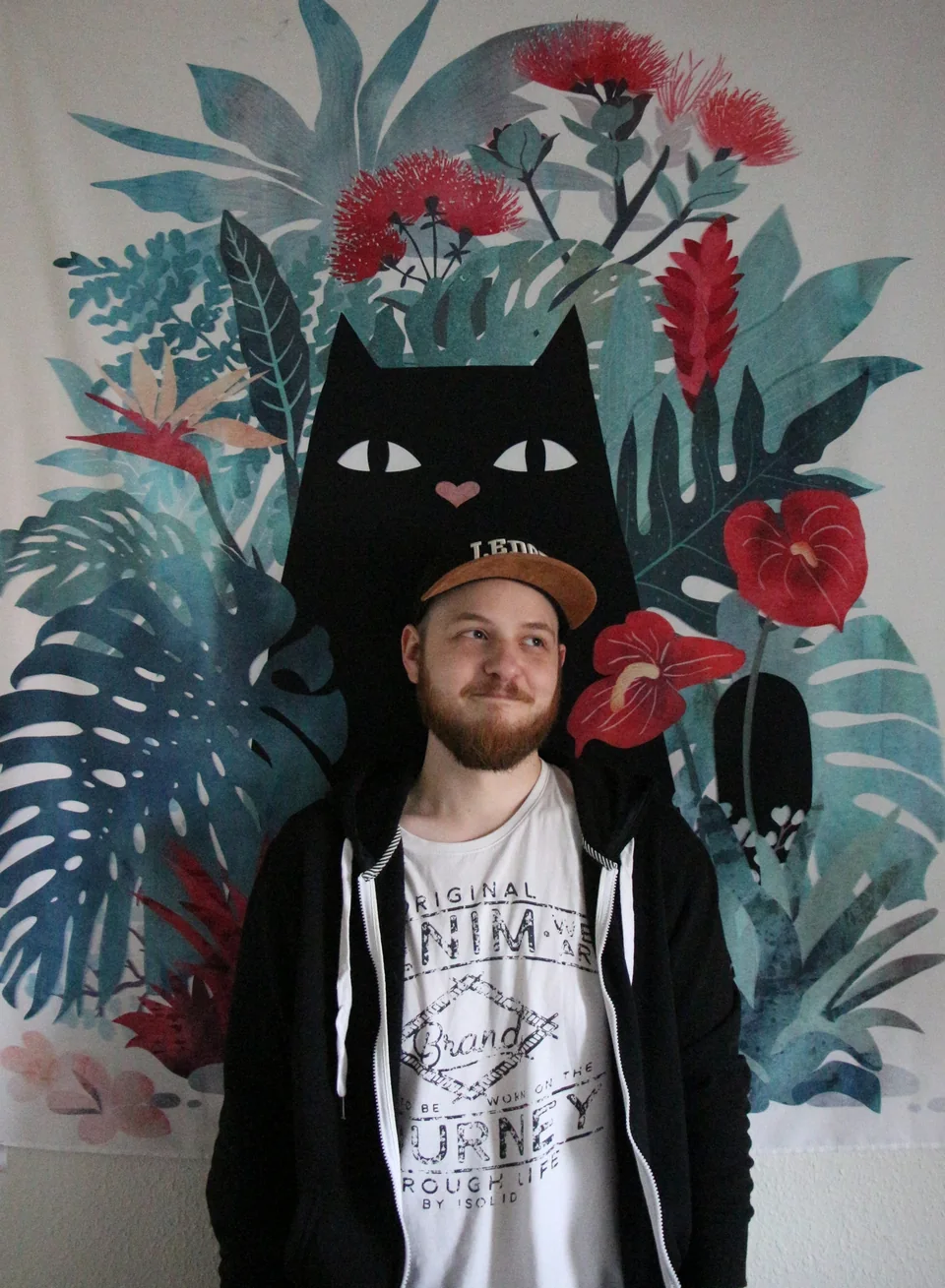 Thomas Ramsing standing in front of a colorful botanical cat mural
